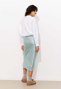 Chemise blanche surdimensionnée associée à une jupe midi en sequins verte menthe, mettant en avant une silhouette élégante et un matériau texturé scintillant. Chaussures et chaussettes brunes.