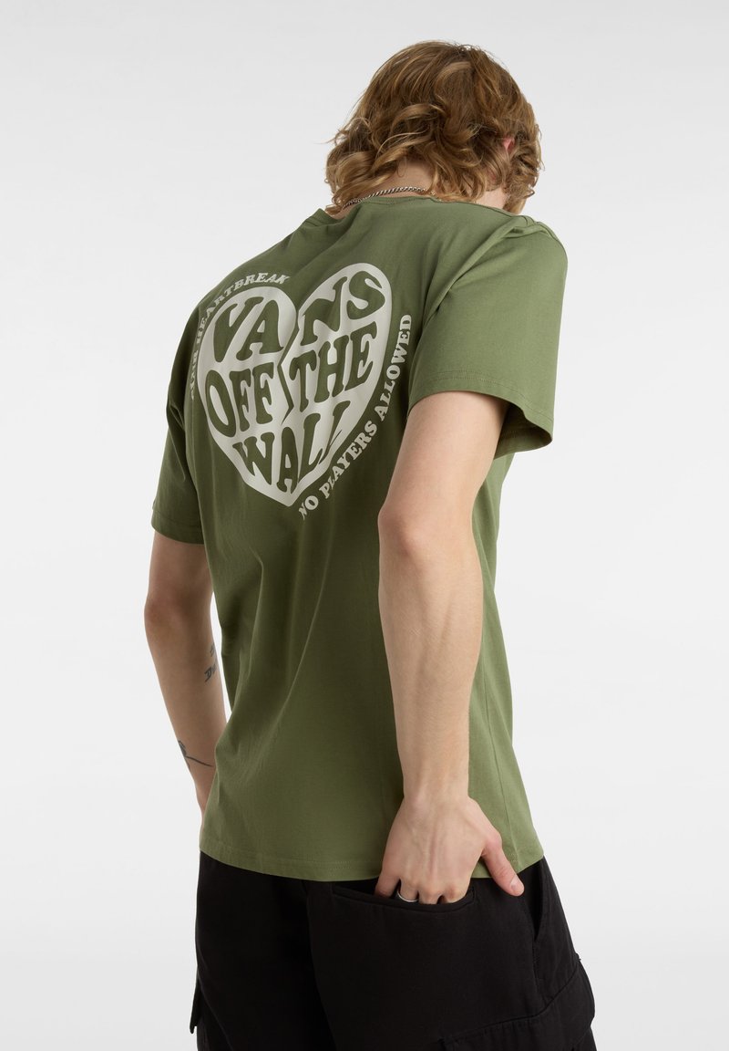Camiseta de algodón verde oliva con un gran gráfico en forma de corazón en blanco que incluye el texto "VANS OFF THE WALL" y "NO JUGADORES PERMITIDOS".