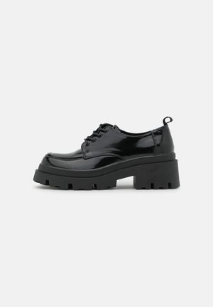 Chaussures en cuir patiné noir avec une semelle épaisse et chunky, dotées de lacets épais. Embout arrondi, détails minimaux et un petit tirant à l'arrière.