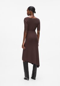 Bruine geribde jurk met korte mouwen en een asymmetrische zoom. Gecombineerd met kniehoge zwarte laarzen. Glad textuur, minimale accenten.