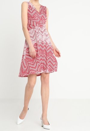 Rood-witte jurk met patroon, V-hals, mouwloos ontwerp, getailleerde taille en uitlopende rok, gecombineerd met witte hoge hakken.