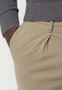 Graue, gerippte Pulloverbündchen über hellbeigen Hosen mit einem gefältelten Abschnitt, gefertigt aus glattem Material mit taillierter Passform.