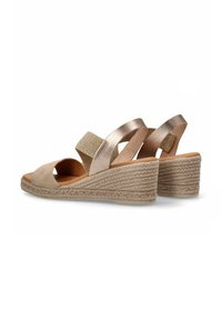 Sandalias de cuña con un suave upper de ante beige, detalles metálicos, bandas elásticas y una suela de plataforma de yute trenzado, diseñadas para la comodidad.