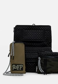 Black textured bags with varying surfaces and patterns; includes a green wallet with branding and contrasting zipper pulls.