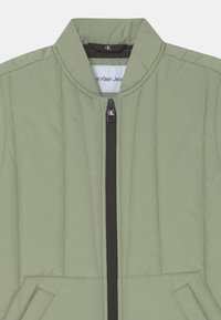 Jasnozielona pikowana kurtka z kołnierzem stojącym i czarnym zamkiem błyskawicznym. Posiada kieszenie boczne oraz metkę wewnątrz z nazwą marki.