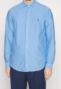 Camicia a maniche lunghe blu e bianca a righe con colletto button-down, dotata di un piccolo logo ricamato sul petto e dettagli con bottoni.