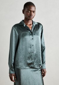 Satin teal bluse med krave, lange ærmer og knaplukning foran. Har en tekstureret overflade og en afslappet pasform.