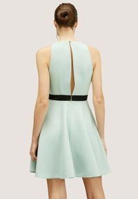 Minttu vihreä hihaton mekko, jossa on tiukka yläosa, levenevä hame, avonaiset selkäyksityiskohdat ja musta vyö. Silkkinen kangas ja rakenne.