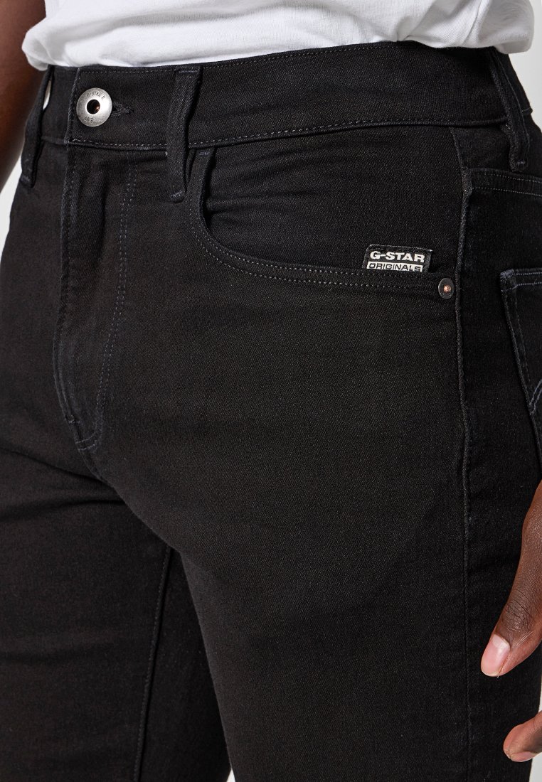 Jeans en denim noir à coupe droite, dotés d'un bouton en métal et d'une étiquette G-Star Originals sur la poche. Texture lisse et design classique.