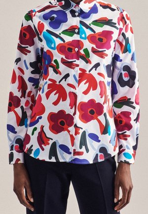 Witte overhemd met kleurrijke abstracte bloemenpatronen in rood, blauw, paars en groen, gedragen met donkere broek.