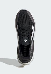 Sneaker atletico nero e grigio con una tomaia in mesh testurizzato, design a tre strisce bianche, punta arrotondata e intersuola bianca imbottita.