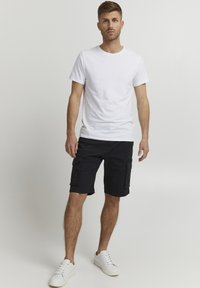T-shirt en coton blanc associé à un short cargo noir de longueur genou avec de multiples poches. Les chaussures sont des baskets blanches. Look simple et décontracté.