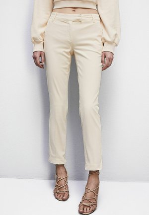Beige-harma broek met een slim fit, zachte stof, rechte benen en zijzakken. Gecombineerd met naaldhakken in huidskleur.