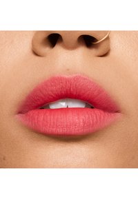 Lèvres roses mates avec une texture lisse et une forme définie, présentant un dégradé subtil. Les dents blanches sont partiellement visibles entre les lèvres.