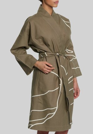 Žena nosi kimono ogrtač boje masline do koljena sa širokim rukavima i bijelim apstraktnim uzorkom linija, vezan u struku pojasom.