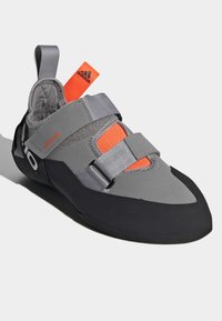 Sapata de escalada com parte superior cinza, seção intermediária laranja e sola de borracha preta. Possui duas correias para um ajuste seguro e calcanhar reforçado.
