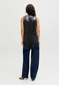 Musta paljettimekko ilman hihoja, jossa on frillimäinen helma, yhdistettynä löysiin tummansinihin farkkuihin, jotka korostavat rentoa istuvuutta ja sileää tekstuuria.