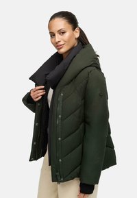 Groene pufferjack met chevronstiksel, zwarte fleece-gekleurde kraag, voorrits en drukknoopsluiting. Bevat een embleem op de mouw.