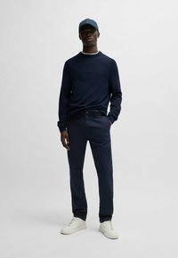 Navy gebreid sweater met geribde manchetten, gecombineerd met navy broek en witte sneakers. Een navy pet maakt de look compleet. Eenvoudig en gestroomlijnd ontwerp.