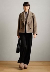 Brown wool double-breasted jacket, black wide-leg pants, striped turtleneck, and beige slippers. Black shoulder bag and smooth texture.