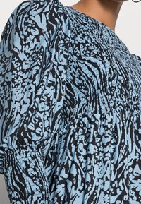 Tissu à motifs noirs et bleu clair, avec des détails smockés et des manches bouffantes, col rond et coupe décontractée.