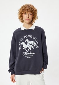 Sudadera azul marino oscuro con estampado gráfico blanco que incluye caballos, texto y un cuello blanco en contraste. Presenta un corte holgado y puños acanalados.