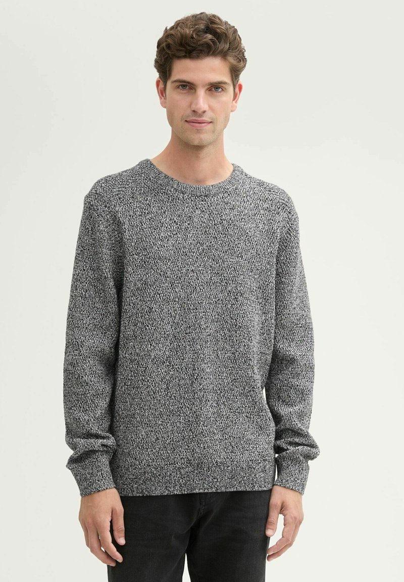 Pull en tricot gris avec un motif texturé, col rond et manches longues, associé à un pantalon foncé. Tissu doux et décontracté.