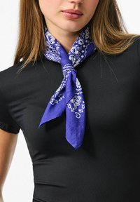 Purple silk scarf with white paisley pattern, tied around the neck, worn over a black fitted top. Smooth texture and vibrant color contrast.