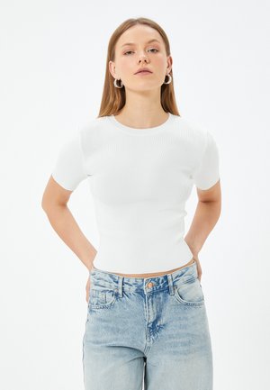 Haut ajusté à manches courtes en ribbed blanc avec un col rond, associé à un jean taille haute bleu clair, doté de poches classiques et d'un bouton.