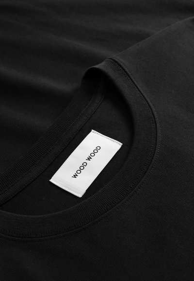 Tricou negru din bumbac, cu decolteu rotund, textură netedă și o etichetă albă pe care este cusut textul "WOOD WOOD".
