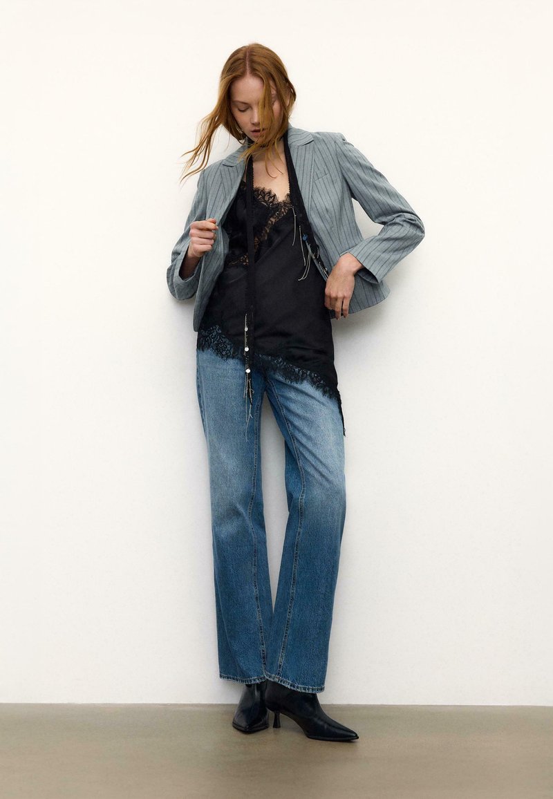 Blazer à rayures grises, caraco en dentelle noire et jean droit bleu clair. Bottines noires complètent la tenue. Fond simple.