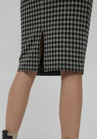 Jupe crayon à motifs damiers noir et blanc avec une fente à l'avant. Fabriquée en tissu structuré, elle présente une coupe droite et un ourlet soigné.