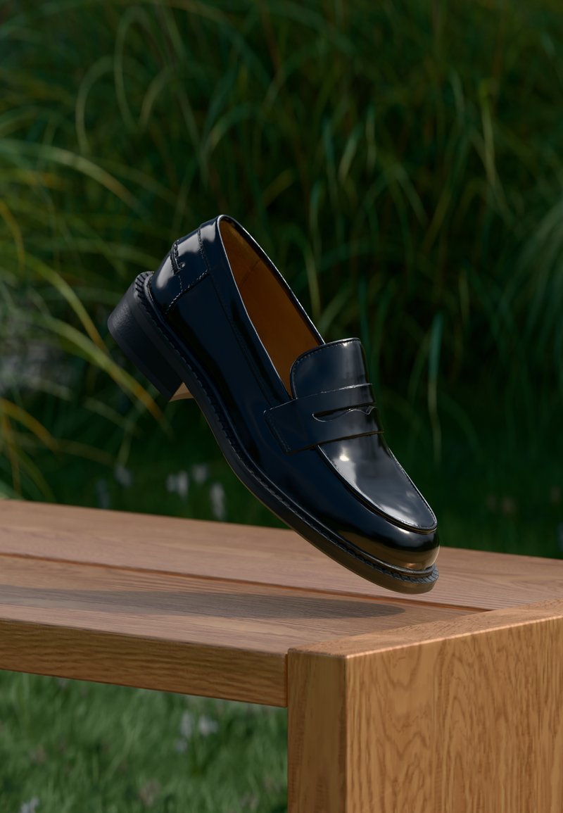 Μαύρο loafer παπούτσι από δέρμα που αιωρείται πάνω από ένα ξύλινο τραπέζι με πράσινα φυτά στο θολό φόντο.