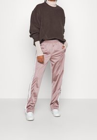 Brązowy, oversize'owy sweter z okrągłym dekoltem, w połączeniu z jasnoróżowymi, satynowymi spodniami dresowymi z białymi bocznymi paskami i elastycznym pasem w talii. Białe sneakersy.