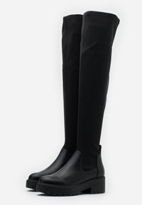 Botas negras por encima de la rodilla con un diseño elegante, hechas de cuero suave y tejido flexible. Presentan una suela de plataforma gruesa.