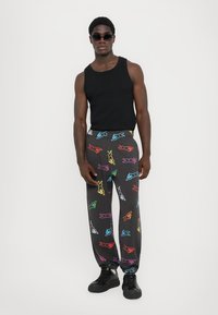 Casual zwart tanktop, kleurrijke cartoon dierenpatronen op grijze joggingbroek, elastische tailleband, taps toelopende pasvorm, gecombineerd met zwarte sneakers.