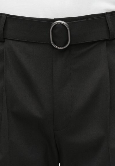 Juodos kelnės su lygiu priekiniu paviršiumi, turinčios plačią diržo kilpą ir stačiakampę metalinę sagtį. Audinys atrodo lygus ir struktūruotas.