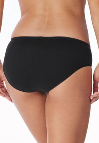 Zwarte katoenen onderbroek met een ribbelstructuur, voorzien van een kanten tailleband en hipster snit, bekeken vanuit de achterkant.