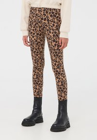 Leggings a stampa leopardata marrone con una vestibilità elasticizzata e una consistenza morbida, abbinati a stivali neri alla caviglia con suola spessa.