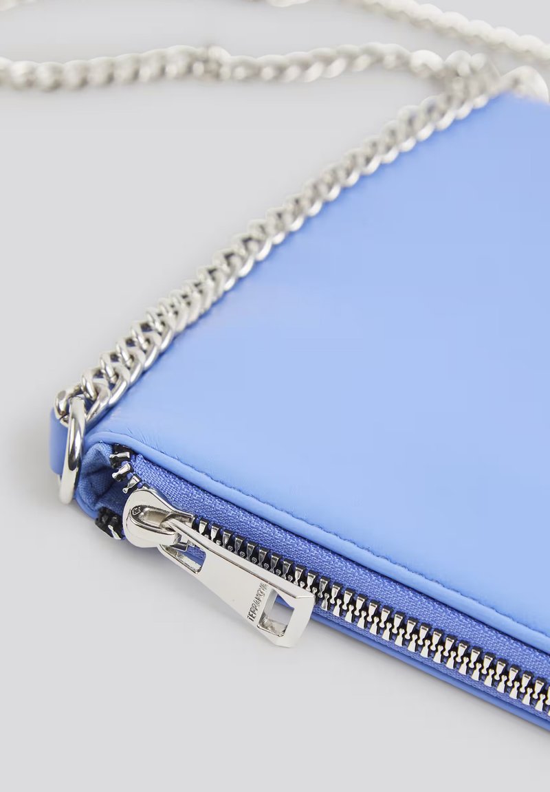 Borsa a tracolla blu in pelle con una tracolla in catena argentata. Presenta una chiusura con zip e cuciture visibili. Texture liscia e forma rettangolare.