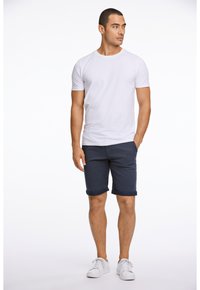 Vit t-shirt med kort ärm som kombineras med mörkblå uppvikta shorts och vita sneakers. Outfiten har en avslappnad, ledig passform.
