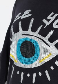 Zwarte stof met een oogontwerp versierd met blauwe, zilveren en gele strassstenen, die textuur en sprankeling benadrukken.
