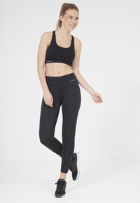 Zwarte sportbh en leggings van rekbaar materiaal, met een aansluitend ontwerp en subtiele branding. Vergezeld van zwarte sportschoenen.