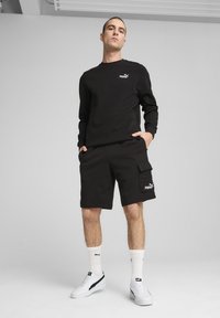 Black sweatshirt and shorts, both made of soft fabric. Notable features include a small Puma logo on the chest and shorts, and cargo pockets.