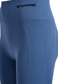Niebieskie legginsy z wysokim stanem, zdobione teksturowanym wzorem z detalami w kształcie chevron i logo na pasie, wykonane z elastycznego materiału.