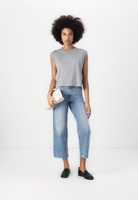 Gray sleeveless top, light blue high-waisted jeans, black loafers, and a beige clutch. Smooth fabric, relaxed fit, wide-leg silhouette.