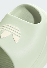 Escorrega moldado verde-claro com superfície texturizada, bordas arredondadas e um design de logotipo em creme contrastante com três riscas.