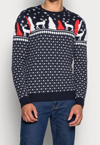 Pull en maille bleu marine orné de flocons de neige blancs, d'arbres rouges et de motifs de rennes, avec des poignets et un ourlet côtelés pour plus de texture et de détail.