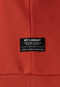 Tessuto arancione con una superficie liscia, contraddistinto da un'etichetta nera con la scritta "KEY LARGO" in bianco e un orlo a coste nella parte inferiore.
