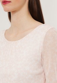 Blusa rosa chiaro con un delicato motivo floreale, dotata di scollo rotondo e maniche lunghe trasparenti, realizzata in un morbido tessuto leggero.